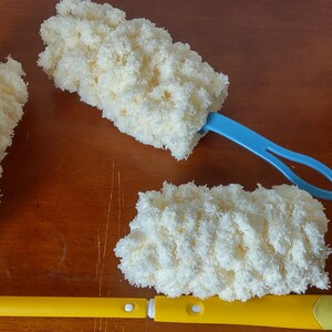 May include: Three cleaning brushes with fluffy, cream-colored microfiber heads. Two have blue handles, and one has a yellow handle. The brushes are designed for cleaning and dusting.