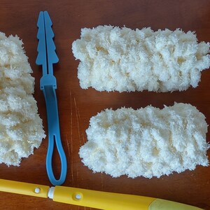 May include: A yellow and white duster with a long handle, a white plastic attachment, and three fluffy, cream-colored cleaning pads. A blue plastic tool is also included. The items are arranged on a wooden surface.