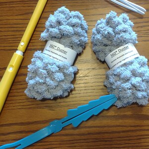 May include: Two gray microfiber dusters with white labels that read "360* Duster Machine Washable and dryable.  Secure prongs together on handle."  The dusters are on a wooden surface with a yellow and white duster handle and a blue plastic handle.