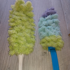 May include: Two dusters with long handles. The duster on the left has a green fluffy head and a white handle with a yellow base. The duster on the right has a blue handle and a fluffy head with purple, blue, and green layers.