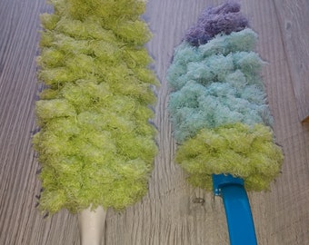 May include: Two dusters with long handles. The duster on the left has a green fluffy head and a white handle with a yellow base. The duster on the right has a blue handle and a fluffy head with purple, blue, and green layers.