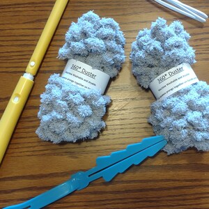 May include: Two gray 360* Duster cleaning tools with white labels that say "Machine Washable and dryable. Squeeze prongs together on handle end." The dusters are on a wooden surface with two blue plastic handles.