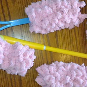 May include: Three pink fluffy dusters with handles. One handle is blue, one is yellow, and one is white.