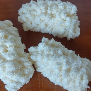 Peut inclure: Trois morceaux de fil de laine rectangulaires, moelleux et blanc cassé, sont disposés sur une surface en bois. La laine semble douce et texturée, avec un aspect dense et nuageux. Les pièces sont probablement destinées à des projets d'artisanat ou de textile.