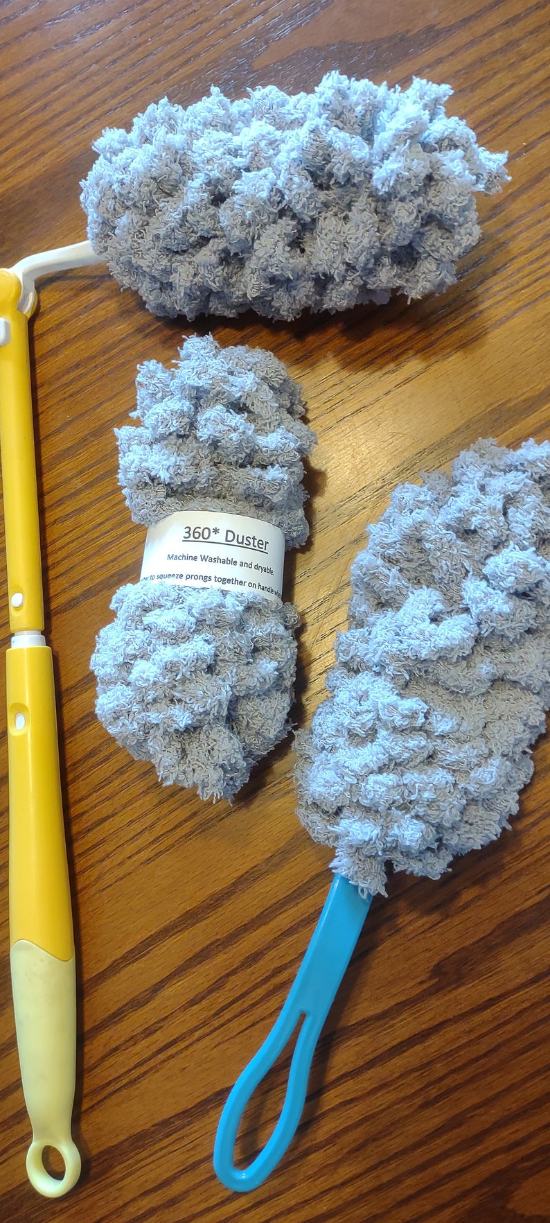 May include: Three gray microfiber dusters with blue and yellow handles. The dusters are machine washable and dryable. The label reads "360* Duster Machine Washable and dryable - to squeeze prongs together on handle w"