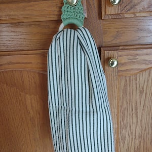 May include: A green crocheted towel ring hanging on a wooden cabinet door with a white and black striped kitchen towel hanging from it.