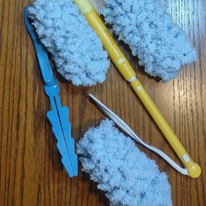 May include: A collection of cleaning tools, including a yellow and blue extendable duster, a blue handle duster, and two light blue microfiber duster heads. The tools are arranged on a wooden surface.