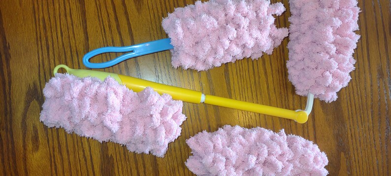 May include: Four pink fluffy dusters with handles. Two dusters have blue handles and two have yellow handles.