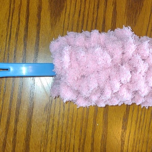 May include: A blue handled duster with a pink fluffy microfiber head. The duster is on a wooden surface.