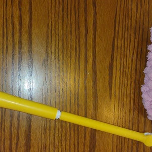 May include: A yellow and white duster with a pink microfiber head. The duster has a long handle and a loop at the end for hanging.