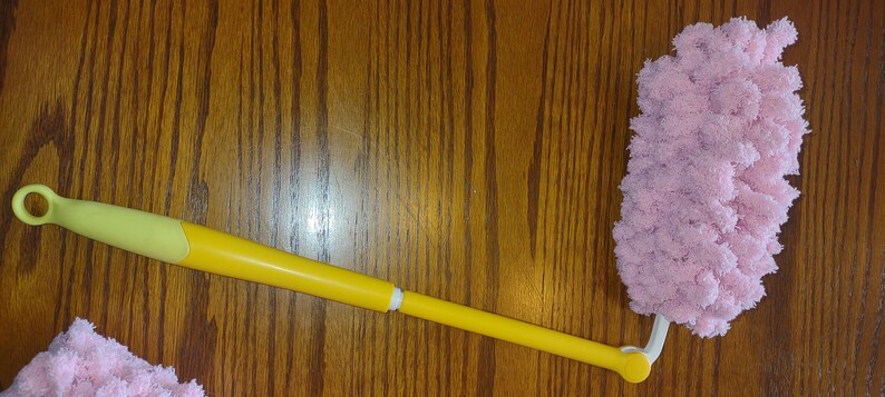 May include: A yellow and white duster with a pink microfiber head. The duster has a long handle and a loop at the end for hanging.