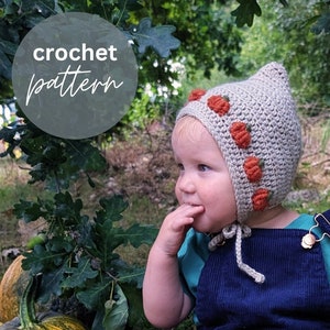 Könnte beinhalten: Eine gehäkelte Kürbis-Mütze mit beigefarbener Basis und orangefarbenen Kürbis-Akzenten. Die Mütze hat einen Bindfaden, der unter dem Kinn gebunden werden kann. Die Mütze wird von einem Kind getragen.