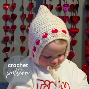 May include: A cream-colored, crocheted baby bonnet with red heart accents. The bonnet has a pointed top and ties under the chin. The words "crochet pattern" are in a circle in the lower left corner.