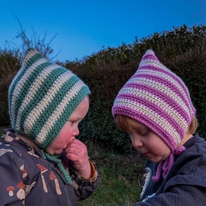 May include: Two children wearing striped crocheted hats. The child on the left is wearing a green and white hat, and the child on the right is wearing a pink and white hat.