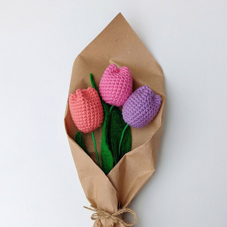 May include: A bouquet of three crocheted tulips in pink, purple, and light pink, wrapped in brown paper with twine.