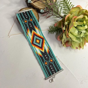 May include: A turquoise, black, white, orange, and yellow beaded bracelet with a geometric pattern. The bracelet has a silver clasp.