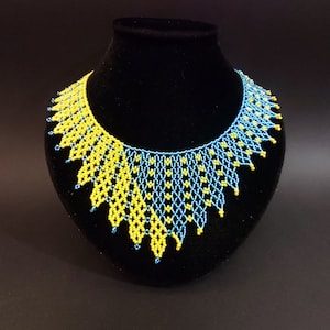 May include: A yellow and blue beaded necklace with a geometric pattern. The necklace is displayed on a black velvet stand.