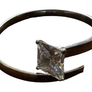 Peut inclure: Une bague en argent avec une seule grande pierre précieuse carrée transparente.