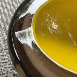 May include: A yellow glass bowl with a dark brown rim. The bowl is made of glass and has a smooth, shiny surface.