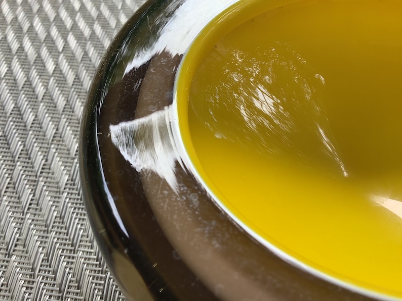 May include: A yellow glass bowl with a dark brown rim. The bowl is made of glass and has a smooth, shiny surface.
