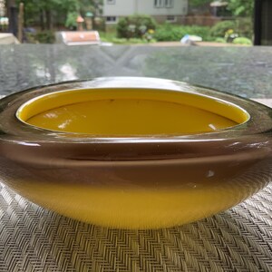 May include: A large, oval-shaped glass bowl with a dark brown rim and a bright yellow interior. The bowl is sitting on a woven placemat.