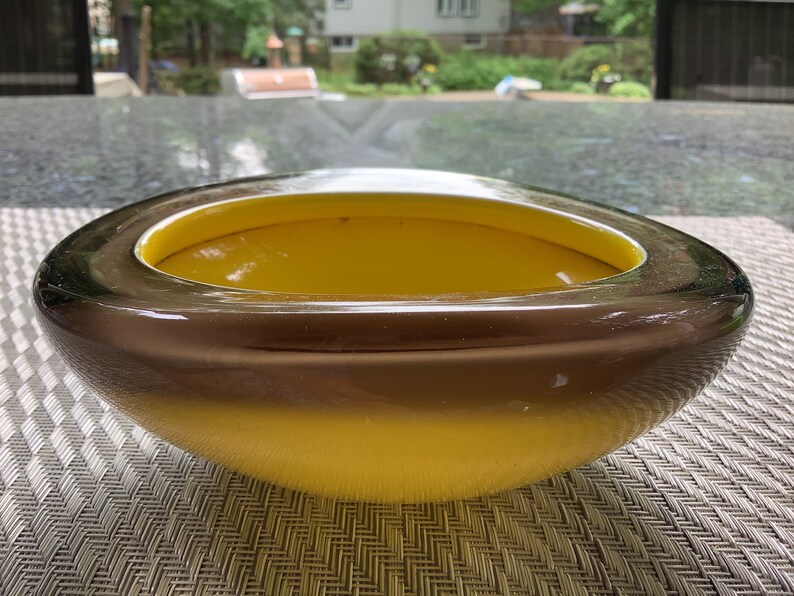 May include: A large, oval-shaped glass bowl with a dark brown rim and a bright yellow interior. The bowl is sitting on a woven placemat.