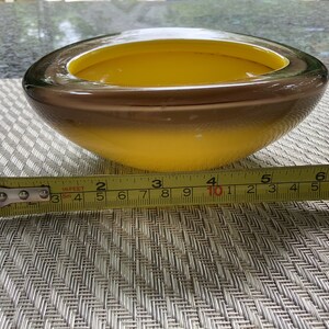 May include: A yellow and brown glass bowl with a rounded shape. The bowl is approximately 10 inches in diameter.