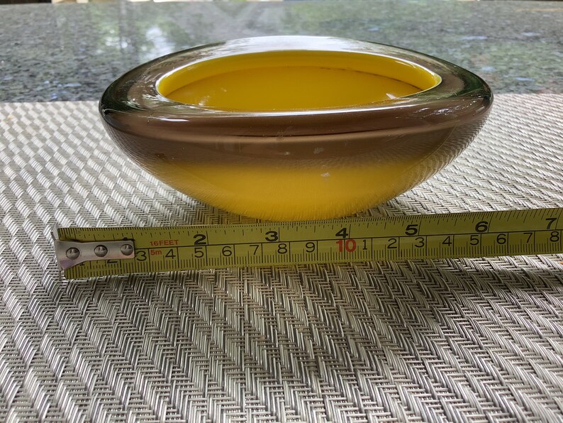 May include: A yellow and brown glass bowl with a rounded shape. The bowl is approximately 10 inches in diameter.