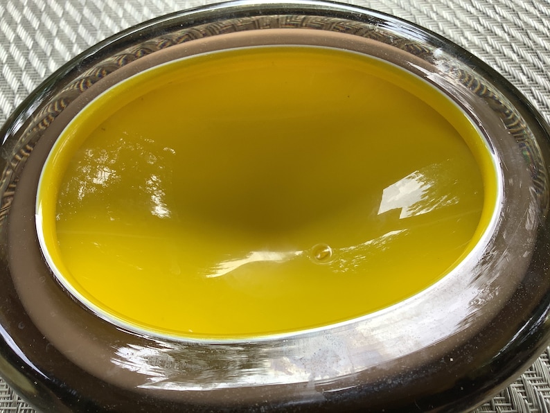 May include: A yellow glass bowl with a brown rim. The bowl is oval shaped and has a smooth, glossy finish.