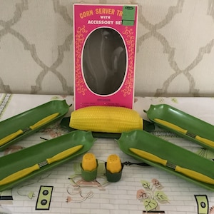 May include: A vintage corn server tray set with green corn cob shaped serving dishes and yellow corn on the cob. The set includes two salt and pepper shakers shaped like corn cobs. The box reads "Corn Server Tray with Accessory Set".