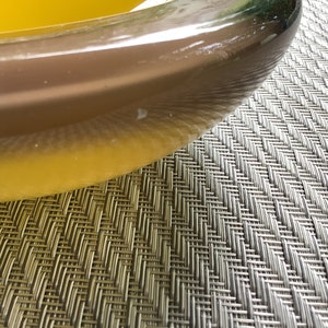 May include: A close-up of a clear glass bowl filled with a bright yellow liquid. The bowl is sitting on a gray woven placemat.