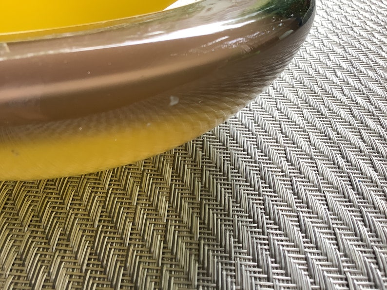 May include: A close-up of a clear glass bowl filled with a bright yellow liquid. The bowl is sitting on a gray woven placemat.