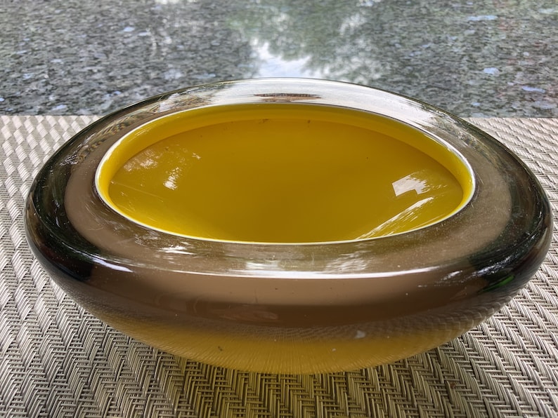 May include: A large, oval-shaped glass bowl with a dark brown exterior and a bright yellow interior. The bowl is made of thick glass and has a smooth, glossy finish.