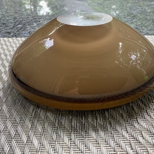 May include: A brown glass bowl with a slightly iridescent finish. The bowl is round and has a wide, shallow shape.