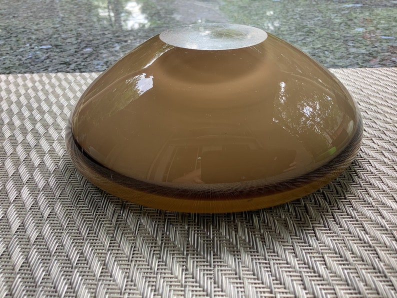 May include: A brown glass bowl with a slightly iridescent finish. The bowl is round and has a wide, shallow shape.