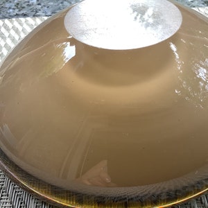 May include: The underside of a large, round, brown glass bowl with a gold rim. The bowl is smooth and reflective.