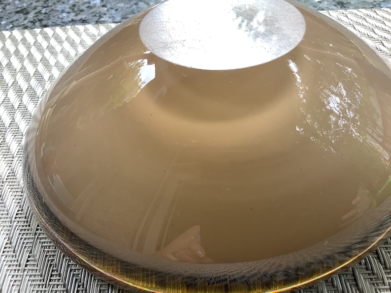 May include: The underside of a large, round, brown glass bowl with a gold rim. The bowl is smooth and reflective.