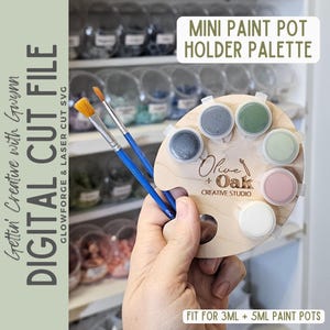 May include: A light-colored wooden paint palette with circular cutouts holding six small paint pots in various colors. The palette features the text Olive + Oak Creative Studio, Mini Paint Pot Holder Palette, and Fit for 3ml + 5ml paint pots.