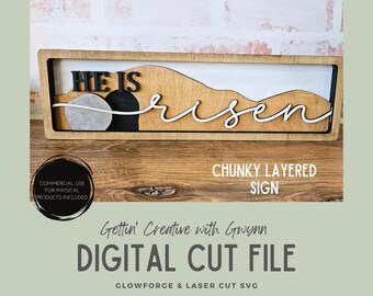 May include: A layered wooden sign with the words "He is Risen" in black and white. The sign features a tomb scene with a circular stone and a mountain range design. The sign is framed in a rectangular wooden border. The words "Chunky Layered Sign" are also visible.