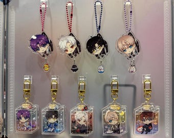 May include: A display of anime-style acrylic keychains. The keychains feature colorful illustrations of characters, some with small charms. The keychains are attached to a clear display board with metal clips. The keychains are in the shape of characters and bottles.