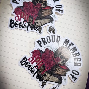 May include: Two white stickers with black text that reads "Proud Member of Spicy BookTok". Each sticker features a skull with a red and black book stack and floral accents.
