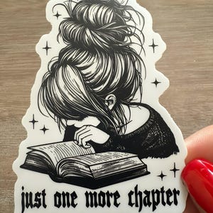 Peut inclure: Autocollant noir et blanc d'une femme avec les cheveux en chignon lisant un livre. L'autocollant porte le texte "just one more chapter" en bas.