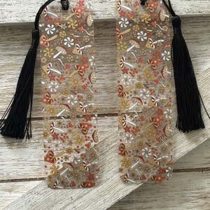 May include: Two clear acrylic bookmarks with a colorful mushroom and flower pattern. Each bookmark has a black tassel.
