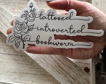 Może przedstawiać: Biała naklejka z czarnym rysunkiem róży i tekstem "tattooed introvert bookworm".