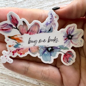 May include: A floral sticker with watercolor-style flowers in shades of pink, purple, and blue. The sticker has the text "buy me books" in a handwritten font across the center.