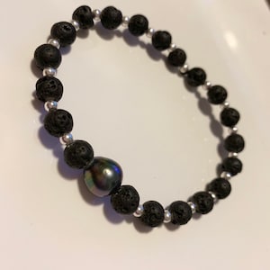 Puede incluir: Pulsera de cuentas de roca de lava negra con cuentas de acento plateadas y una sola perla gris oscura. La pulsera está ensartada en un cordón flexible y está diseñada para usarse alrededor de la muñeca.