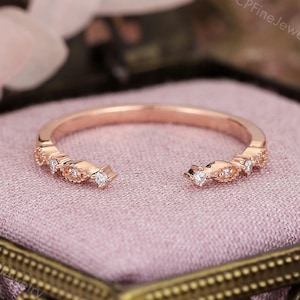 May include: Rose gold ring with a delicate open design. The ring features small, sparkling diamonds and intricate detailing along the band. The ring is displayed in a decorative jewelry box with a pink interior, showcasing its elegant design.