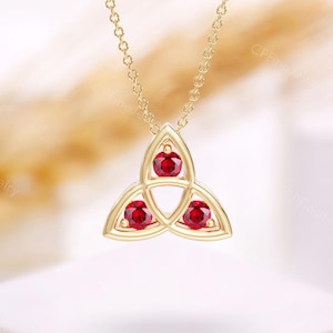 Może przedstawiać: Złoty naszyjnik z zawieszką w kształcie celtyckiego węzła ozdobioną trzema czerwonymi kamieniami szlachetnymi.