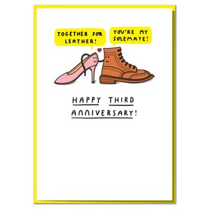 May include: A greeting card featuring a cartoon illustration of a pink high heel shoe and a brown leather boot. The shoe says "Together for leather!" and the boot says "You're my Solemate!" The card reads "Happy Third Anniversary!"
