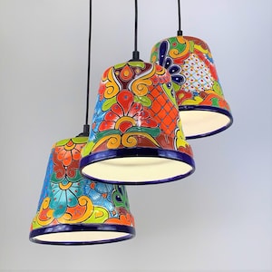 May include: Three colorful ceramic pendant lights with floral patterns in shades of blue, green, orange, red, and yellow. The lights are hanging from a black metal ceiling fixture.